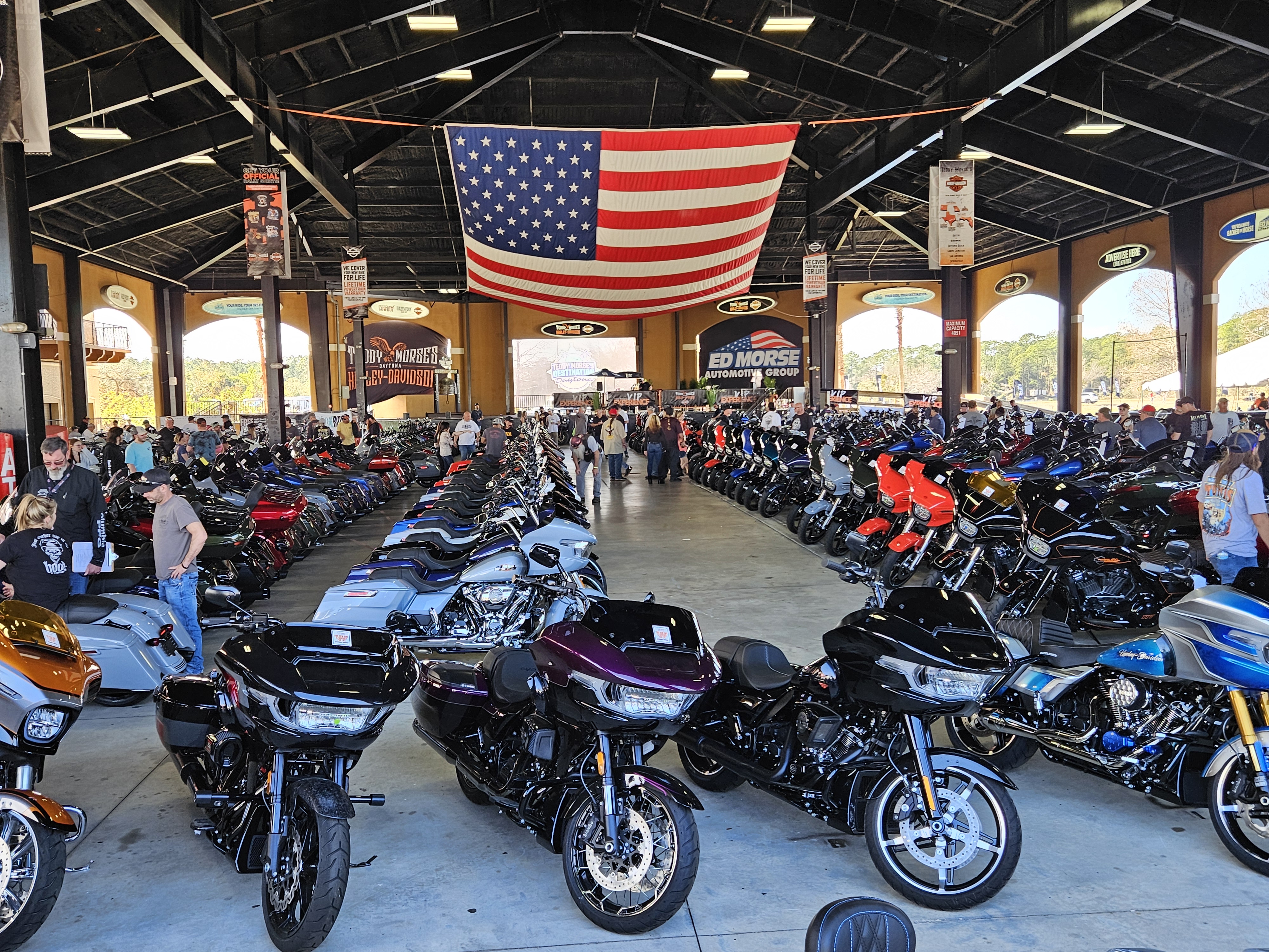 Rows of baggers under the covered pavilion at Destination Daytona with a giant American flag overhead
